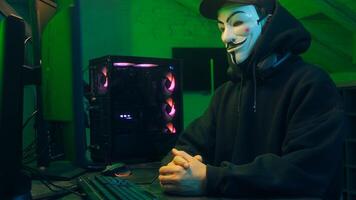 Lviv, Ukraine - June 03, 2024. Masked man anonymous stretching fingers programmer hacking typing computer malware networks web danger scam database spy system virus theft server break cryptocurrency photo