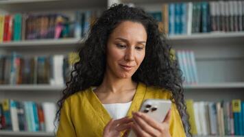 Latin Hispanic Arab woman student mobile phone user smartphone texting sms chatting gadget library university high school college networking smile female girl laugh technology browsing e-learning web photo