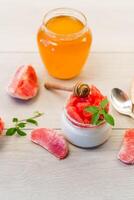 homemade sweet yogurt in a glass jar with pieces of red ripe grapefruit and honey, on a wooden table photo