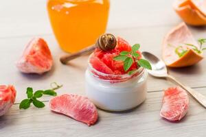 homemade sweet yogurt in a glass jar with pieces of red ripe grapefruit and honey, on a wooden table photo