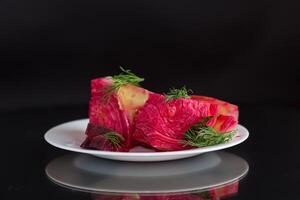 pickled cabbage with beets and carrots, in a plate, isolated on black background photo