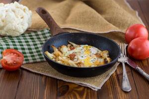 fried omelette with cauliflower and vegetables in a frying pan on a wooden table photo