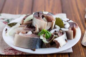 salted mackerel with onions and spices, in a plate on a wooden table photo