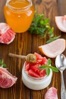 homemade sweet yogurt in a glass jar with pieces of red ripe grapefruit and honey, on a wooden table photo