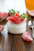 homemade sweet yogurt in a glass jar with pieces of red ripe grapefruit and honey, on a wooden table photo