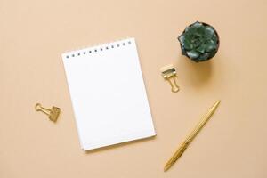 Open Notepad with a blank sheet of paper, ballpoint pen, succulent and paper clips on a beige background. Workplace of a freelancer or office worker photo
