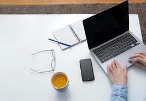 Person using a laptop computer on the modern white office desk table top view. photo