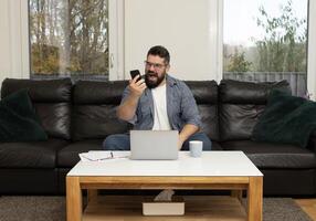 Angry stressed man yelling on his phone call with a burnout face expression while working at the home office. photo