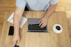 Man using a laptop on the wooden desk table top view. photo