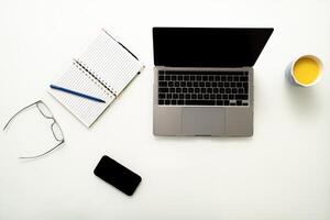 Modern white office desk table with laptop computer, phone, glasses, notebook and cup of juice top view with copy space, flat lay. photo