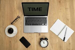 Business working time concept, word time on the screen laptop, glasses, coffee, notebook, clock, phone, laptop on the wooden desk top view. photo
