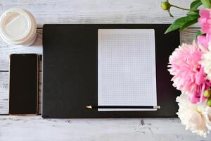 The image shows a white wooden table with various objects placed on it.A black laptop with a black notebook and a black pencil resting on it is placed in the center photo