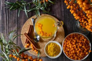 A flatlay shot showcasing a white rustic wooden surface with bowls filled with sea buckthorn berries, lemon slices, honey, and cloves. photo