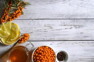 A flat lay of ingredients for a healthy and flavorful drink, including sea buckthorn berries, lemon slices, honey, and cloves, all displayed on a rustic wooden background. photo