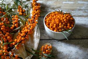 This image features a white rustic wooden surface adorned with a selection of natural ingredients, including sea buckthorn berries, lemon slices, honey, and cloves. photo
