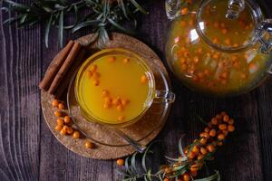 This image features a rustic white wooden surface with a selection of ingredients for a refreshing and flavorful drink, including sea buckthorn berries, lemon slices, honey, and cloves. photo