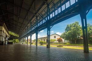 The historic Ambarawa Railway Museum features a platform with a metal roof, surrounded by lush greenery and charming buildings. Indonesia, 17 November 2024 photo