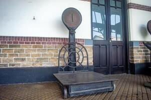 An antique weighing scale with a circular dial and a metal platform, set against a brick wall, Indonesia, 17 November 2024 photo