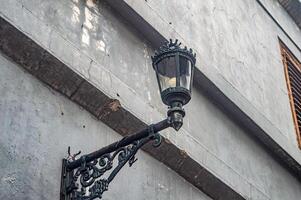 A vintage street lamp mounted on a weathered wall with intricate metalwork, showcasing urban decay and historical charm photo