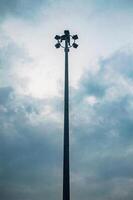 A tall street light pole with multiple floodlights against a cloudy sky, creating a dramatic and moody atmosphere photo
