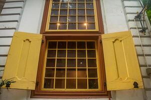 A vintage window with yellow shutters and a grid pattern, set in a white wall with decorative trim, creating a charming and rustic look photo