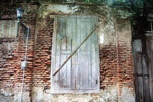 Old, weathered wooden door on a brick wall with a diagonal support beam, vintage street lamp, and creeping vines photo