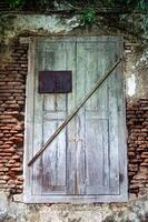 An old wooden door with peeling paint, secured by a rusty metal bar, set in a weathered brick wall with creeping vines photo
