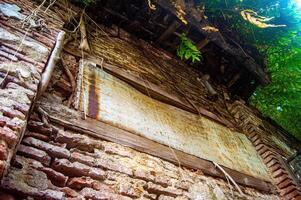 An old, abandoned brick building with overgrown vegetation and a rusty metal sheet, showcasing decay and nature reclamation photo