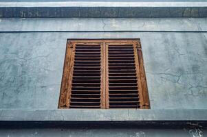 An old, weathered wooden window shutter on a cracked, faded blue wall. The rustic charm and aged texture make it a captivating subject for vintage and architectural photography photo
