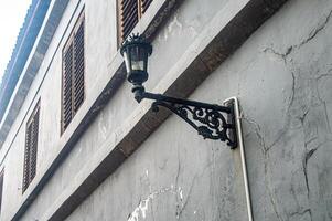 A vintage street lamp with intricate wrought iron design is mounted on an old, weathered building with wooden shutters, highlighting the rustic charm of historical architecture photo
