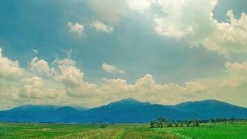 Stunning landscape of lush green fields with a backdrop of majestic mountains under a vibrant blue sky with fluffy clouds. Perfect for nature, travel, and outdoor themes photo