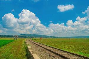 Scenic railway track through lush green fields under a vibrant blue sky with fluffy white clouds, perfect for travel and nature themes photo