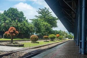 Scenic railway station platform with lush greenery and vibrant trees under a clear blue sky, perfect for travel and nature themes photo