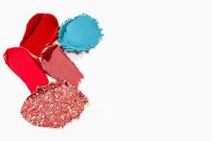 Cosmetic textures of lipstick, eyeshadow, bronzer, glitter, and powder in a colorful composition with empty space on a light white background. photo