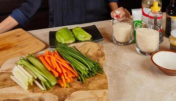 A beautifully arranged wooden board with sliced vegetables, avocado, and sushi rice in glasses, set for sushi making in a kitchen. photo