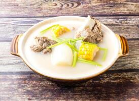 Radish and Pork Bone Pot with corn and scallions served in broth isolated on wooden table side view of hong kong food photo