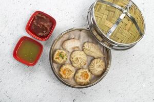 Assorted Steamed Momo or Dumplings including chicken, cheese, mushroom with mayo dip and tomato sauce served in bamboo steamer on white background top view of bangladeshi, indian and chinese dim sum photo