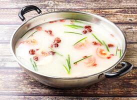 Creamy Tomato Hot Pot Soup topping with scallions and red dates or jujube served in steel pot isolated on wooden table side view of hong kong food photo