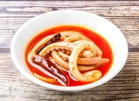 Spicy squid tentacles with red chilli served in bowl isolated on wooden table side view of hong kong food photo