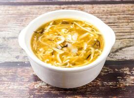 Hot and sour wild pepper Noodles soup with egg and mushroom served in broth isolated on wooden table side view of hong kong food photo
