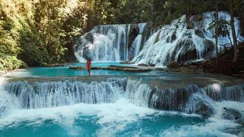 Woman in bikini walking on scenic cascade waterfalls with blue water in Sulawesi, drone view video