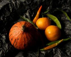 oranges, tangerines, chili peppers and pumpkin on a black background, craft paper photo