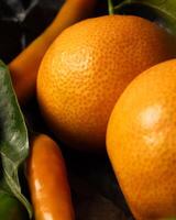 oranges, tangerines, chili peppers and pumpkin on a black background, craft paper photo