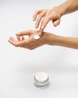 Female hands apply cream white jar with cream stands on background photo