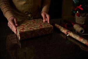 Hands carefully wrapping a holiday gift with festive paper on a table photo