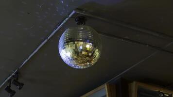 A close-up view of a glittering disco ball reflecting light patterns, suspended from the ceiling of a dimly lit interior with visible cables and industrial details video
