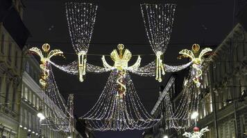 Intricately designed Christmas decorations with illuminated crowns and angelic figures hang above a historic street in Saint Petersburg. Strings of fairy lights create a magical canopy, enhancing the video