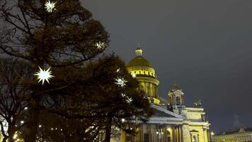 Sparkling star-shaped lights adorn the trees near St. Isaac's Cathedral, creating a magical festive ambiance on a winter evening in Saint Petersburg. The golden dome contrasts beautifully with the video