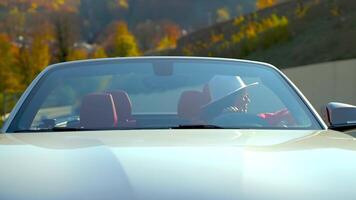 lady in white convertible car in sunny autumn day in mountain, frontal view against natural scenery video