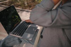 A person is sitting on a bench with a laptop open in front of them. They are typing on the keyboard, possibly working or browsing the internet. Concept of productivity and focus. photo